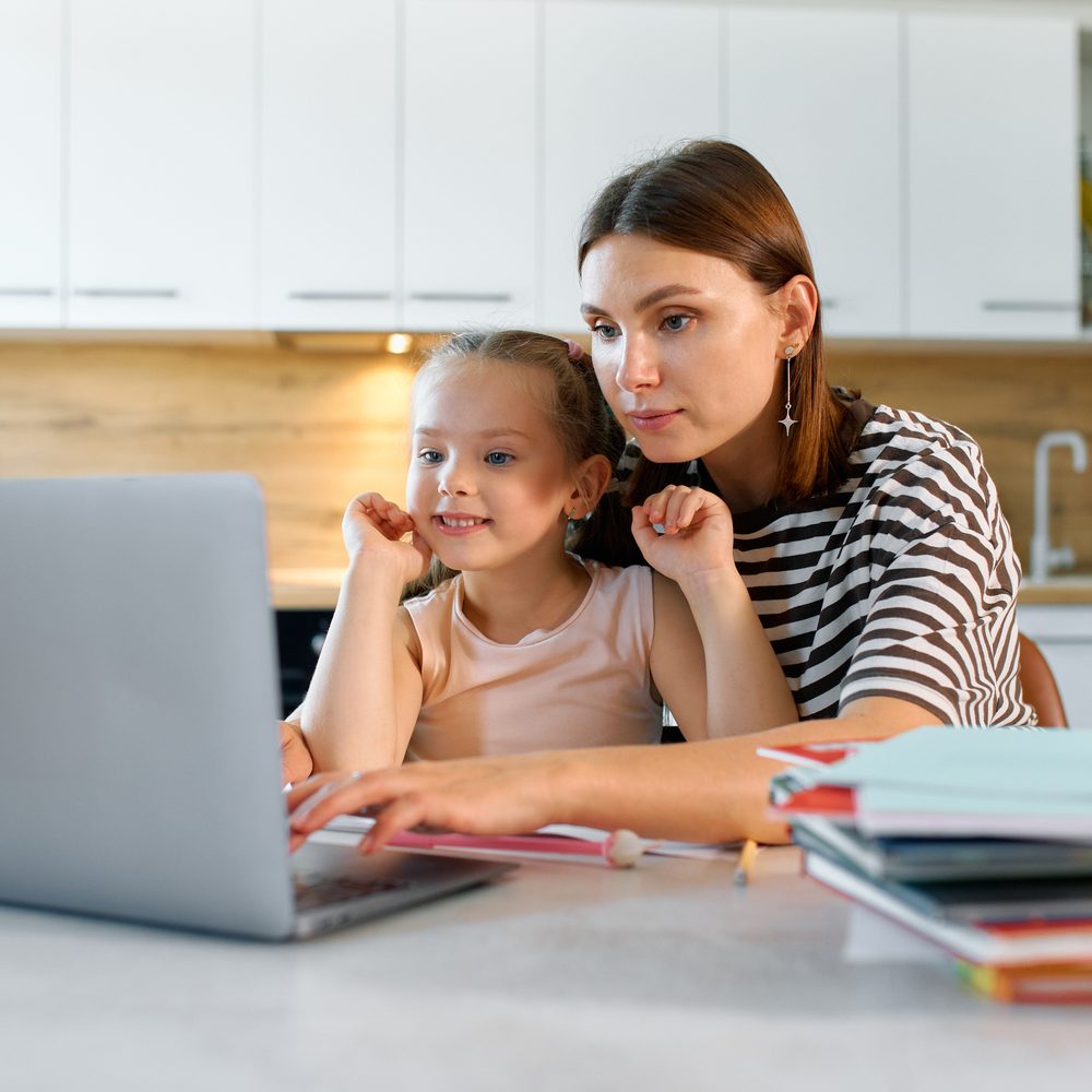 Mutter und Tochter sitzen am Küchentisch vor dem Laptop, die Mutter tippt