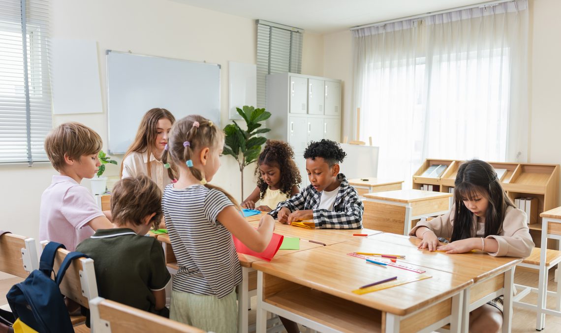 Eine Betreuerin bastelt mit einer Gruppe Grundschulkinder an einem Tisch mit buntem Papier